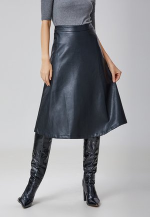 Jupe en cuir noir en forme de A avec une texture lisse, taille haute et longueur genou, associée à des bottes high-tech brillantes à motif crocodile.