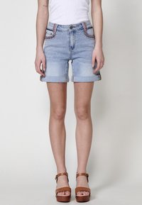 Shorts en denim bleu clair avec des ourlets roulés, ornés d'accents brodés sur les poches avant, associés à des sandales à plateforme marron.