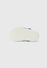 Vit sneakersula med texturerade greppmönster, med en blå och svart övre sektion. Designen inkluderar en framträdande logotypkontur.