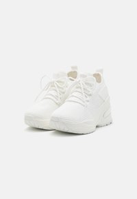 Białe siatkowe sneakersy o teksturowanej powierzchni, płaskich sznurowadłach i wyściełanej podeszwie. Charakteryzują się minimalistycznym wzornictwem i pętelką na pięcie.