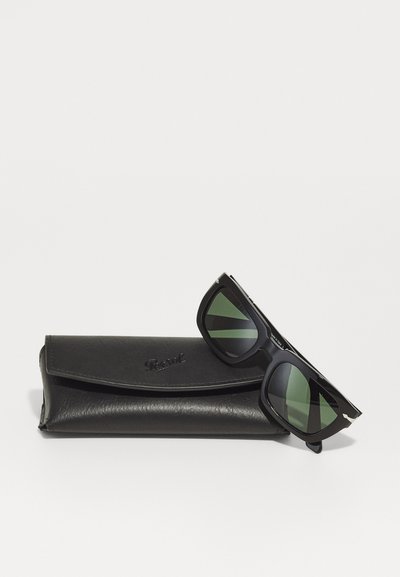 Occhiali da sole neri con lenti verdi e forma rettangolare, abbinati a un elegante astuccio in pelle nera con logo impressa.