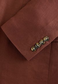 Manche de blazer marron avec quatre boutons style écaille cousus en rangée près du poignet.