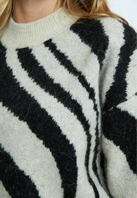 Maglione a maglia con collo a costine. Presenta strisce a zebra bianche e nere, una texture morbida e un aspetto accogliente.