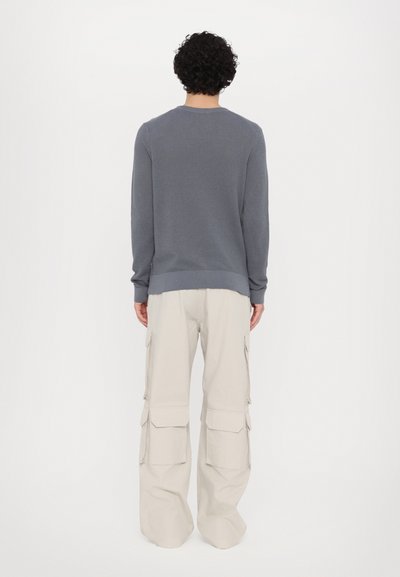 Grauer Rippstrickpullover mit Rundhalsausschnitt, kombiniert mit beigefarbenen Cargo-Hosen, die über mehrere seitliche Taschen und einen weit geschnittenen, lockeren Sitz verfügen.