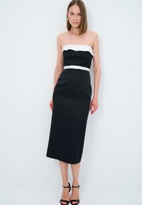 Abito midi nero senza spalline con scollatura bianca a scallop, corpetto aderente e cintura bianca. Tessuto liscio e design minimalista.