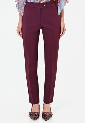 Donna che indossa pantaloni slim-fit color bordeaux su misura e décolleté abbinate con punta appuntita, con una camicetta floreale parzialmente visibile.