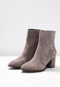 Szare zamszowe botki za kostkę z wąskim noskiem i 10-centymetrowym słupkowym obcasem. Posiadają boczny zamek błyskawiczny oraz kontrastowe przeszycia wzdłuż szwów.
