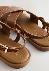 Sandali in pelle marrone con cinturini incrociati, dotati di cinturini in suede beige, hardware in metallo dorato e suola imbottita per il massimo comfort.
