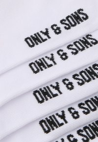 Vita bomullsstrumpor med svart broderad text "ONLY & SONS" som upprepas flera gånger. Mjuk textur och avslappnad design.