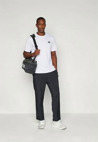 Geantă duffel neagră cu logo "adidas", tricou alb cu un logo mic, pantaloni închiși la culoare și sneakers albi. Design simplu și croială casual.