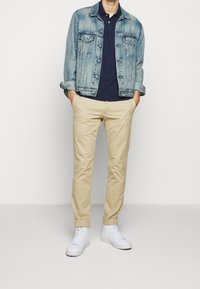 Jeansjacka i ljusblå, marinblå polo, beige chinos och vita högstövlar. Jackan har knäppningar och bröstfickor.