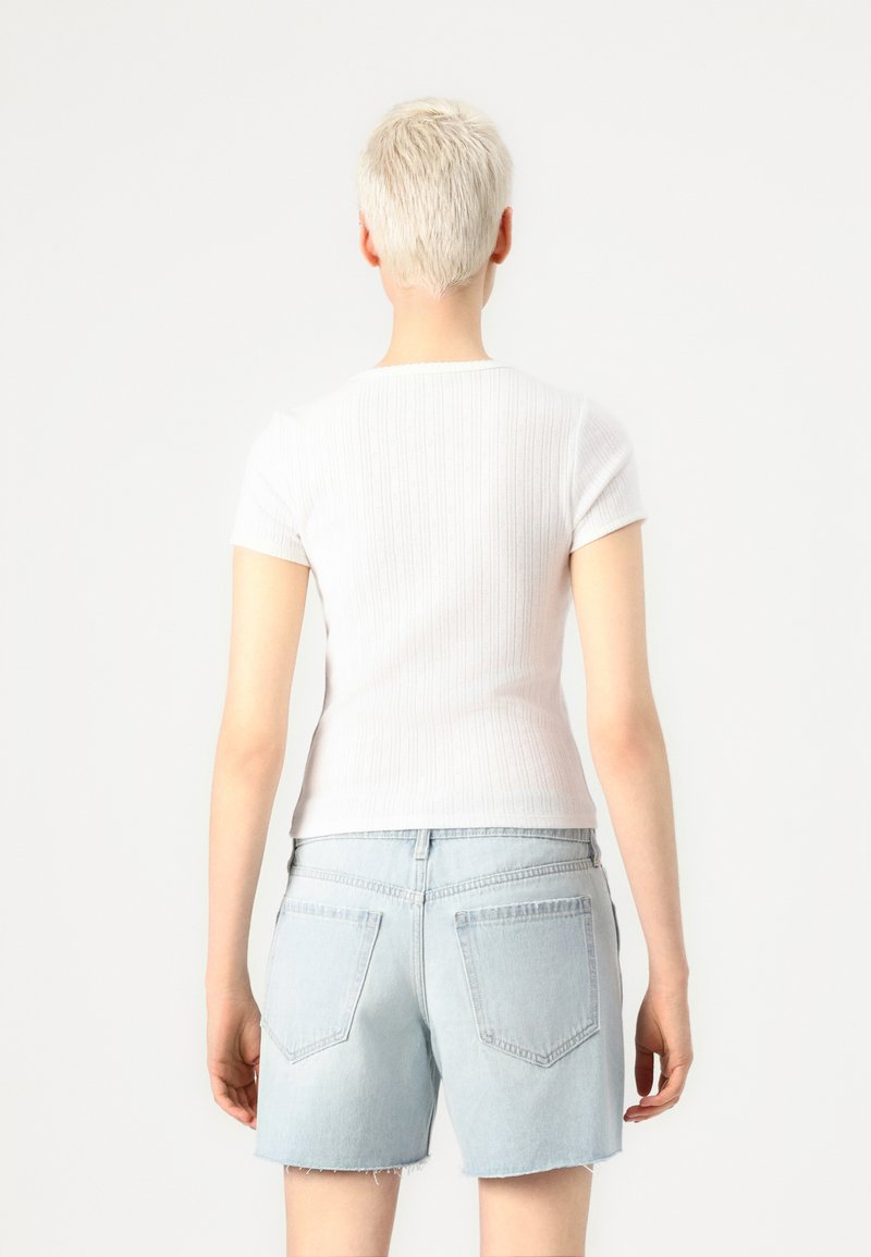 Biały chabrowy top z krótkim rękawem połączony z jasnoniebieskimi szortami dżinsowymi, prezentujący dopasowany krój i postrzępiony dół szortów.