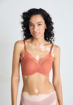 Kant bralette in koraal met verstelbare bandjes, voorzien van een semi-doorzichtig ontwerp en golvende randen, gecombineerd met lichtroze ondergoed.