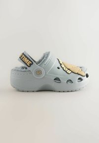 Light blue clog with fuzzy lining, featuring cutouts and a playful ice cream design on the top. Adjustable black strap with text.