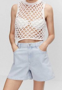 Bílý háčkovaný crop top s diamantovým vzorem, skombinovaný se světle modrými pruhovanými šortkami bílé barvy, které mají přední kapsy a zapínání na knoflík.