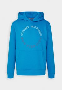 Sudadera azul con bolsillo canguro, que presenta un diseño circular con el texto "TOMMY HILFIGER" y "NEW YORK CITY". Textura de tela suave.