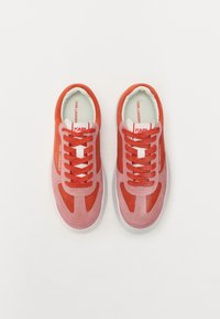 Røde og rosa semskede sneakers med gummisåler, snørebånd og branding på tungen, med en glat tekstur og sporty silhuett.