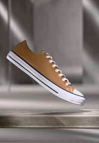 Gele leren sneaker met witte veters, zwart-witte strepen op de zool, ronde neus en contrasterende witte rubberen kap.