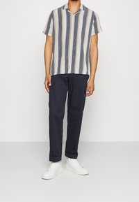 Koszula z krótkim rękawem w pionowe niebieskie i kremowe paski, z guzikami, w połączeniu z granatowymi spodniami i białymi trampkami, charakteryzująca się luźnym krojem.