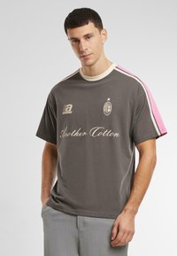 Šedé bavlněné tričko s krátkým rukávem, se růžovými akcenty na ramenech, logem a stylizovaným textem na přední straně. Hladká textura, uvolněný střih.