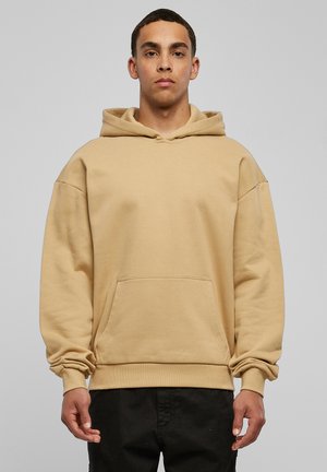 Beige hoodie made of cotton, featuring a large front pocket, drawstring hood, and ribbed cuffs and hem. Simple, relaxed-fit design.