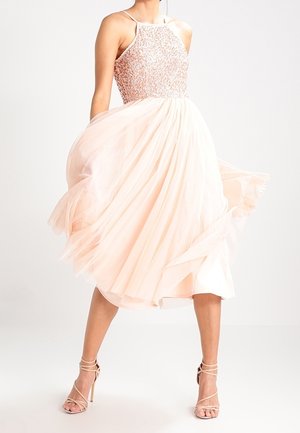Sukienka do kolan z koralikowym gorsetem i zwiewną warstwową spódnicą z tiulu w delikatnym różowym kolorze. Do stroju dobrano sandały na paski.