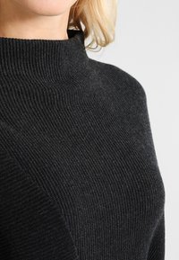 Black, ribbed knit sweater with a high, folded neckline. Soft texture; features diagonal seam detail across the front.