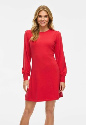 Robe rouge à manches longues avec un col rond, buste ajusté et jupe évasée. Tissu doux et lisse avec des manches bouffantes.