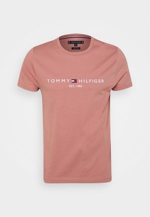 Camiseta de algodón rosa con cuello redondo, con "TOMMY HILFIGER EST. 1985" impreso en blanco, con un acento de logo azul y rojo.