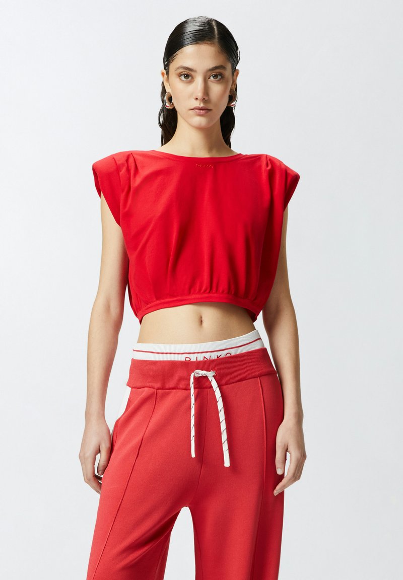 Top corto rosso con maniche a cappuccio e orlo arricciato, abbinato a pantaloni sportivi rossi con cordoncino e vita elastica bianca.