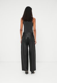 Zwarte leren wijde broek met een hoge taille, achterzakken en een gladde textuur, gecombineerd met een aangesloten zwarte tanktop.