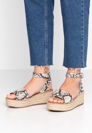 Voeten dragen sleehakken met slangenprintbandjes en enkelbandjes met gespen, gecombineerd met blauwe cropped jeans met rafelige zomen.