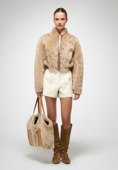 Beige fluffy cropped jakke med pelsstruktur, parret med cremede shorts, knæhøje brune suede støvler og en matchende taske.