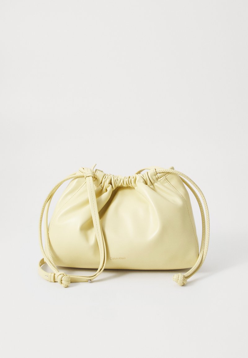 Bolsa de couro amarela com um design franzido, fecho com cordão ajustável e uma única alça longa. Branding minimalista na parte inferior.