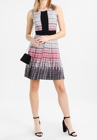 Šaty bez rukávů s černým pasem; mají gradientní vzor v růžové a fialové, rozšiřující se sukni a hladkou texturu látky.