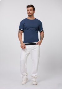 Navigatieblauwe T-shirt met korte mouwen en witte en zwarte gestreepte manchetten; gecombineerd met witte broek en witte sneakers. Glad textuur, casual pasvorm.