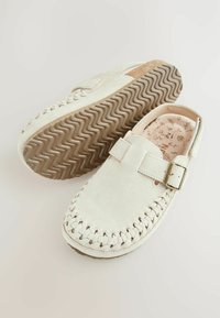 Ballerines en daim blanc avec des détails tissés et une seule sangle dotée d'une boucle en métal. Intérieur clair à motifs et semelle en caoutchouc texturé.