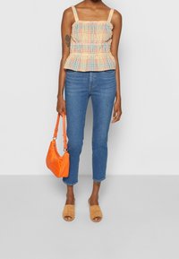 Peplum top s multikulturním kostkovaným vzorem, modrými a oranžovými akcenty, spárovaný s modrými džíny s vysokým pasem a tan skluznými sandály. Oranžová kabelka.