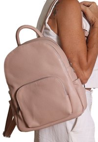 Zaino in pelle rosa con forma arrotondata, superficie testurizzata, tasca anteriore con zip e doppie spalline. Presenta una maniglia superiore per un facile trasporto.