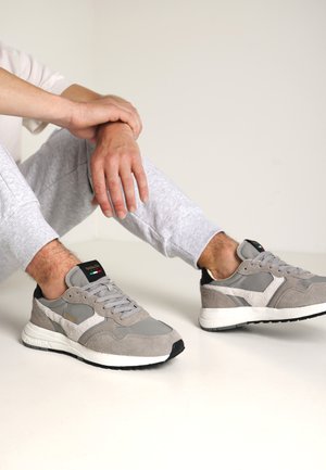Scarpe sportive grigie in suede e mesh, con un accento sul tallone nero, suola chiara e logo ricamato sulla linguetta.