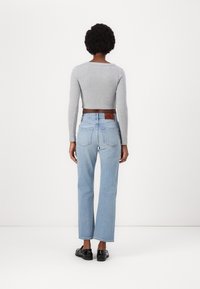 Maglia grigia a maniche lunghe e corta, abbinata a jeans chiari a vita alta, con una patch in pelle marrone e un design dritto, vista da dietro.