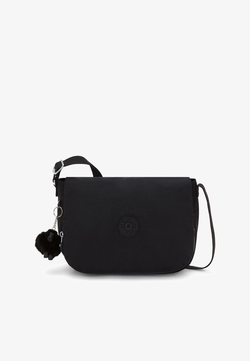 Černá crossbody kabelka vyrobená z odolné tkaniny s klopou, obsahující kulatou nášivku, stříbrné kovové doplňky a černou pom-pom ozdobu.
