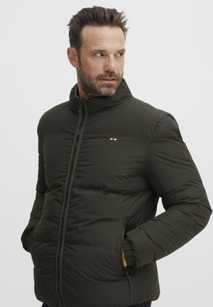 Donkergroene pufferjack met een hoge kraag, een rits aan de voorkant en zijzakken. Heeft een klein logo met rode, witte en blauwe accenten.