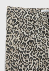 Pantalons en jean avec imprimé léopard, base beige clair, taches brun foncé, design à cinq poches et accents métalliques sur les poches.