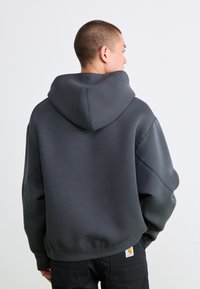 Mørkegrå hættetrøje med stor hætte, faldne skuldre og ribbede manchetter. Glat tekstur og minimalistisk design. Mærke synligt ved kanten.
