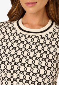 Strickpullover mit einer cremefarbenen Basis und einem schwarzen geometrischen Muster, rundem Rippkragen und glatter Textur.