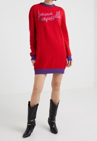 Red knitted sweater dress with purple ribbed cuffs and neckline, featuring the text "Amour impossible" in a contrasting pink.