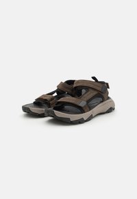 Brune utendørs sandaler med svarte stropper, borrelås-lukking og teksturerte såler; designet for komfort med et holdbart og robust utseende.