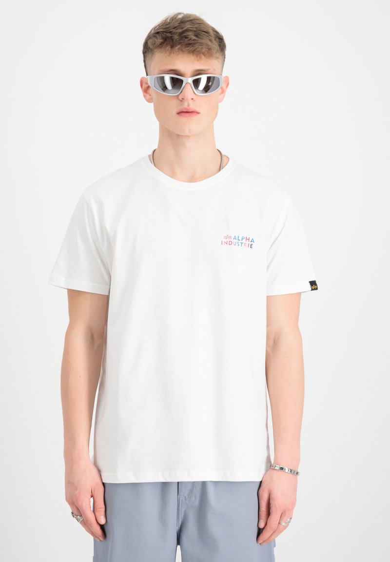 Camiseta de algodón blanca con un pequeño logo multicolor de "ALPHA INDUSTRIE" en el pecho, combinado con elegantes gafas de sol plateadas.