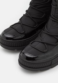 Bottes d'hiver noires à lacets avec embouts brillants et semelles épaisses texturées sur fond blanc.